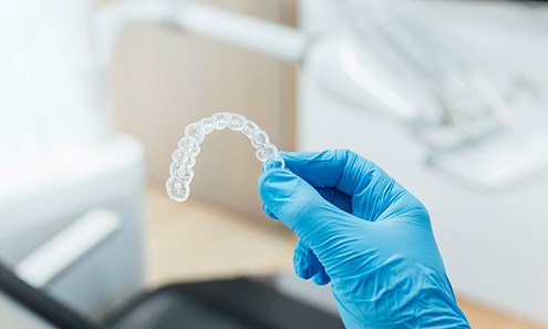 Dentist with blue glove holding clear aligner