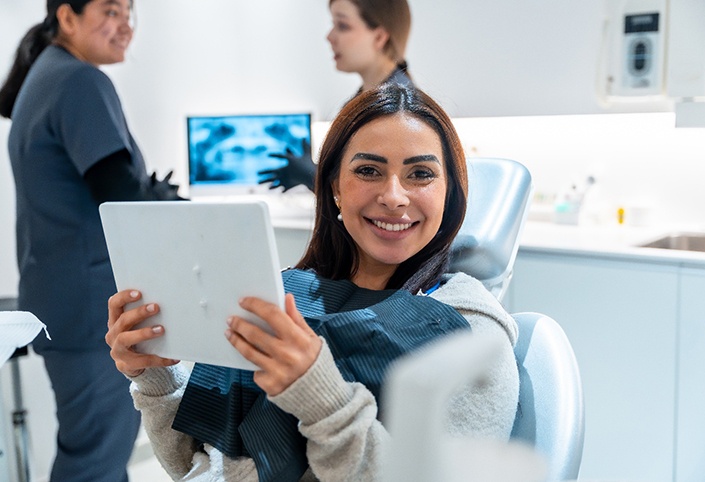 Patient smiling while holding mirror in treatment chair