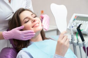 Patient looking at herself in handheld mirror in dentist’s chair.