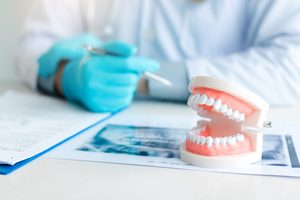 Dentist's gloved hands at desk with paperwork, X-rays, and model teeth